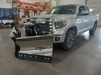An angled view of a silver truck with a Fisher EZ-V v-plow attached