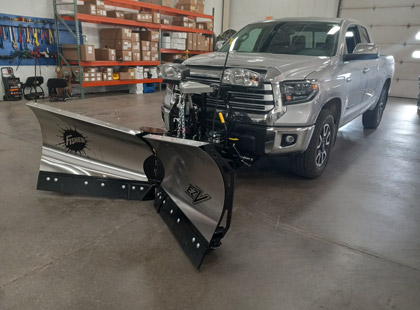 An angled view of a silver truck with a Fisher EZ-V v-plow attached